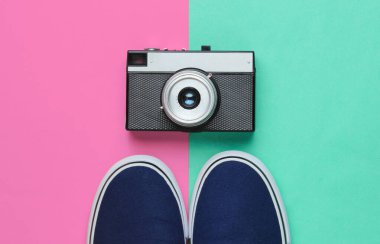 Hippi stili düz yatıyordu. Klasik spor ayakkabıları ve pastel renkli arka planda retro film kamerası. Üst görünüm