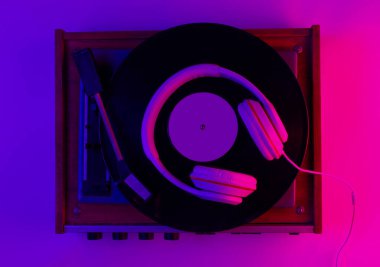 Retro tarzı müzik konsepti. Klasik kulaklıklar, gradyan pembe neon ışıklı vinil plak çalar. Popüler kültür. 80 'ler. Üst görünüm