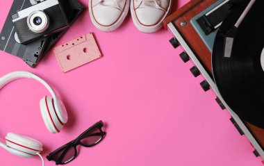 80 'lerin pop kültür objeleri dümdüz uzanıyordu. Vinil çalar, kulaklıklar, ses kaseti, video kasetler, film kamerası, pembe arka planda spor ayakkabıları. Uzayı kopyala Üst görünüm