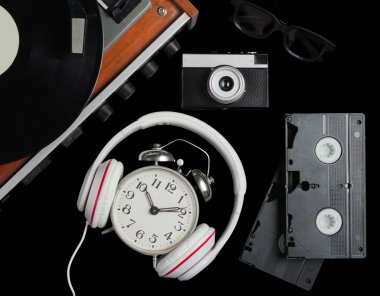 80 'lerin pop kültür objeleri dümdüz uzanıyordu. Vinil çalar, kulaklıklar, video kasetler, çalar saat, siyah arka planda film kamerası. Üst görünüm