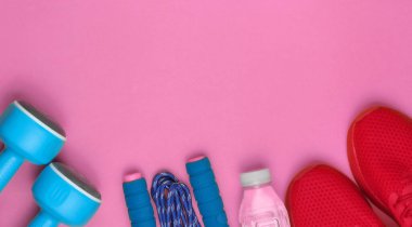 Pembe arka plan eğitimi için ekipman. Spor ayakkabılar, ip atlama, dambıllar, bir şişe su. Düz yatış stili. Üst Manzara. Boşluğu kopyala