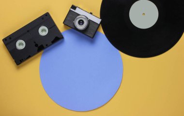 Retro vinil kayıt, video kaset, sarı arka planda mavi daireli film kamerası. Üst görünüm