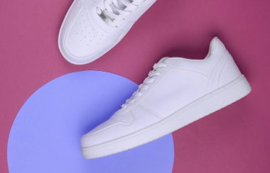 Pembe arka planda beyaz spor ayakkabılar ve mor pastel daire. Gençlik hipster konsepti. Üst görünüm