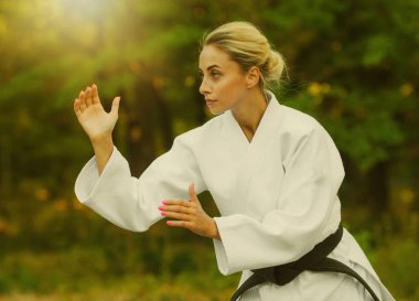 Beyaz kimonolu, siyah kuşaklı çekici kadın dövüşçü açık havada dövüşüyor.