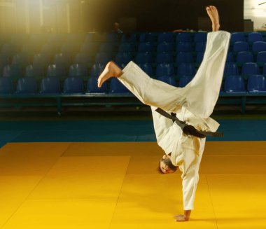 Beyaz kimonolu sporcu spor salonunda capoeira çalışıyor.