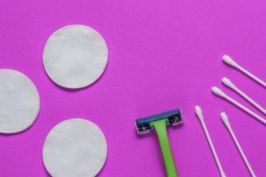 Güzellik hayattır, minimalizm. Pamuk çemberli plastik epilator jilet ve mor arka planda kulak çubukları. Güzellik hizmetleri için kadın aksesuarları. Üst görünüm