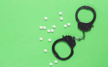 Tıptaki yozlaşma kavramı. Yeşil arka planda haplar ve kelepçeler. Tıbbî hayat. Suçun cezası. Üst görünüm