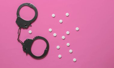 Tıptaki yozlaşma kavramı. Pembe arka planda haplar ve kelepçeler. Tıbbî hayat. Suçun cezası. Üst görünüm