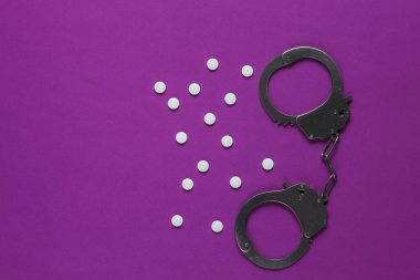 Tıptaki yozlaşma kavramı. Mor arka planda haplar ve kelepçeler. Tıbbî hayat. Suçun cezası. Üst görünüm