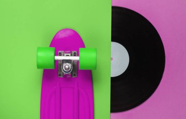 Retro tarzı. Plastik mini kruvazör tahtası ve renkli arka planda vinil plak. Yaz eğlencesi. Gençlik minimalist konsepti. 80 'ler. Üst görünüm