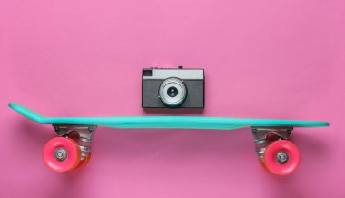 Retro tarzı. Plastik mini kruvazör tahtası ve pembe arka planda retro kamera. Pastel renk eğilimi. Yaz eğlencesi. Gençlik minimalist konsepti. 80 'ler. Üst görünüm