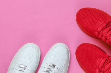 Pembe arka planda iki çift spor ayakkabı. Beyaz ve kırmızı ayakkabılar. Üst görünüm