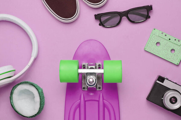Hipster outfit. Skateboard with headphones, audio cassette, retro camera and sneakers on pink background. Creative fashion minimalism. Minimal summer fun. Pop art. 80s.