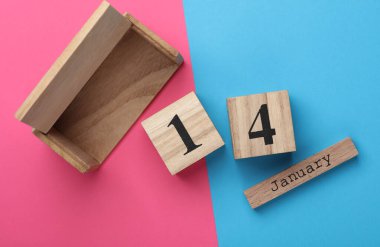 14 Ocak tarihli ahşap blok takvimi pembe mavi arka planda. Üst görünüm