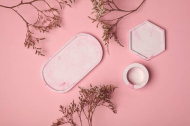 Kurumuş çiçekli pembe arka planda farklı şekillerde dekoratif pembe alçı tepsiler. Kozmetik veya mücevher için mum düzenleyicileri anlamına geliyor. Üst görünüm