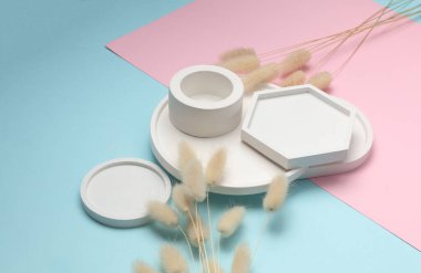 Mavi pembe pastel arka planda, kuru çiçeklerle dekoratif beyaz alçı tepsiler. Kozmetik veya mücevher için mum düzenleyicileri anlamına geliyor. Üst görünüm