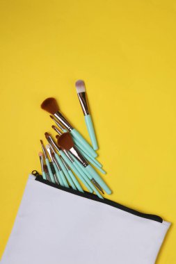 Sarı arka planda makyaj fırçası olan beyaz kumaş kozmetik çanta. Tasarım için model