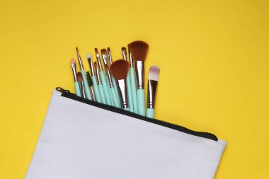 Sarı arka planda makyaj fırçası olan beyaz kumaş kozmetik çanta. Tasarım için model