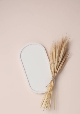 Alçıtaşı oval tepsisi ve pastel arka planda kuru buğday kulakları.