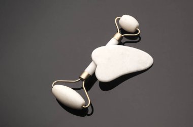 Beyaz yeşim silindir ve siyah arka planda gua sha kazıyıcı