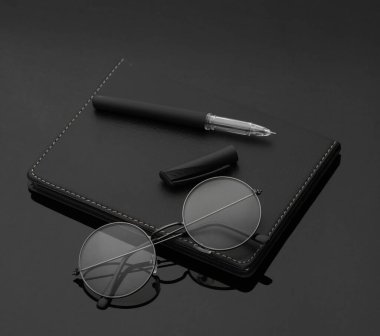 Siyah arka planda siyah kalem ve gözlüklü siyah deri defter.