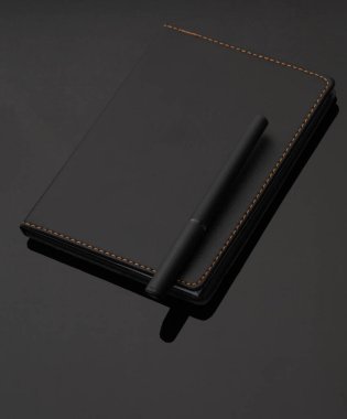 Siyah arka planda siyah deri defter ve kalem.