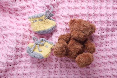 Pembe arka planda yeni doğan bebek ve oyuncak ayı için örgü ayakkabılar.