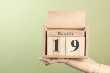 Tahta blok takvimi ve tarihi 19 Mart. Yeşil arka plandaki kuklanın elinde.