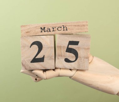 Tahta blok takvimi ve tarihi 25 Mart. Yeşil arka plandaki kuklanın elinde.