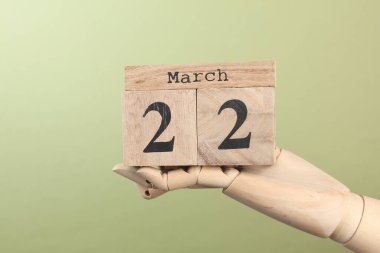 Tahta blok takvimi ve tarihi 22 Mart. Yeşil arka plandaki kuklanın elinde.