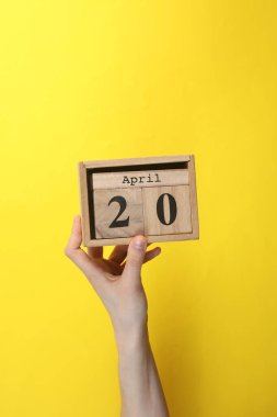 20 Nisan tarihli ahşap blok takvimi sarı arka planda.