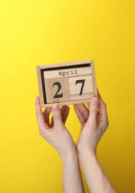 Ahşap blok takvimi ve sarı arka planda 27 Nisan tarihi.