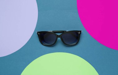 Mavi arka planda renkli kağıt daireli şık güneş gözlükleri. Düz moda natürmort hayat. Üst görünüm