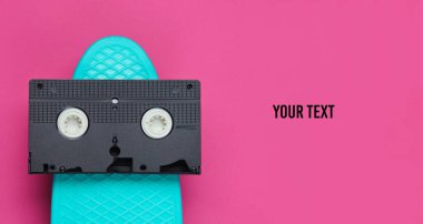 Pop sanatının retro tarzı hala hayat. 80 'ler. Kruvazör tahtası ve video kaset pembe kağıt arka planda, mesajınız için yer var. Yaz eğlencesi. Üst görünüm.