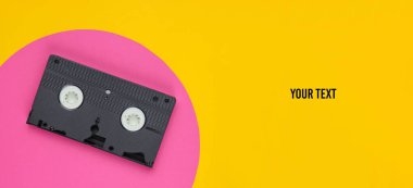 Sarı arkaplanda pembe daireli video kaset ve mesajın için yer. Stüdyo moda çekimi. 80 'ler, popüler kültür. Üst görünüm.