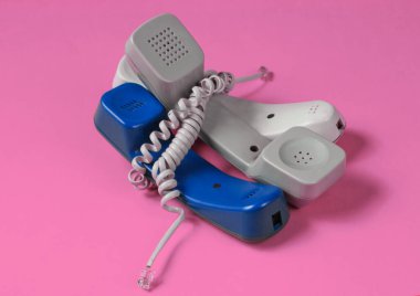Pembe stüdyo arka planında kabloya sarılı üç ofis telefonu tüpü. Çağrı merkezi, yardım hattı kavramı