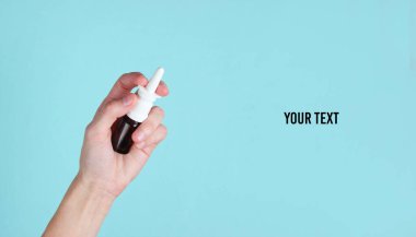 Kadın eli, mavi bir arkaplanda burun spreyi tutuyor. Metnin için yer var.