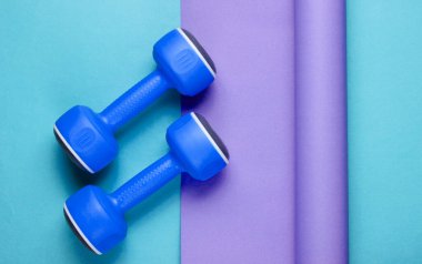 Ambalajlı kağıdın üzerinde mavi plastik halterler. Renk trendi, minimalist spor ve moda natürmort. Üst görünüm