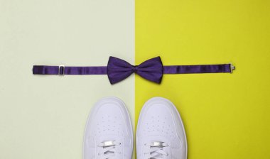 Beyaz spor ayakkabı ve papyon, arka planda iki renkli kağıt. Minimalist moda konsepti. Üst görünüm