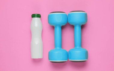 Minimalist diyet ve spor konsepti. Dambıllar, pembe kağıt üzerine bir şişe yoğurt. Üst görünüm