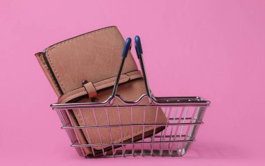 Minimalist alışveriş konsepti. Pembe arka planda cüzdanı olan küçük bir alışveriş sepeti.