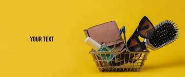 Minimalist alışveriş konsepti. Sarı arka planda kadın aksesuarları olan mini alışveriş sepeti. Sapı kopyala