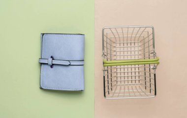 Minimalist alışveriş konsepti. Renkli arka planda mini alışveriş sepeti ve deri cüzdan. Üst görünüm