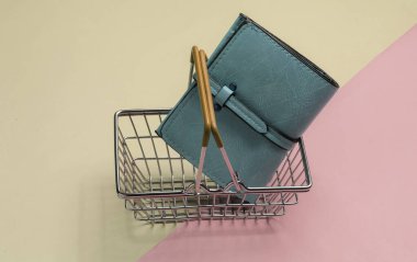 Minimalist alışveriş konsepti. Renkli arka planda mini alışveriş sepeti ve deri cüzdan..