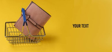 Minimalist alışveriş konsepti. Sarı arka planda mini alışveriş sepeti ve deri cüzdan. Boşluğu kopyala