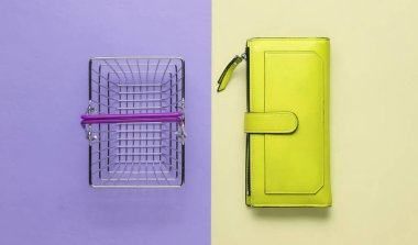 Minimalist alışveriş konsepti. Mini alışveriş sepeti ve mor sarı arka planda yeşil deri cüzdan. Üst görünüm