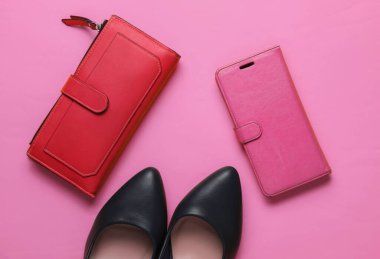 Stüdyo moda çekimi. Yüksek topuklu ayakkabılar, kırmızı cüzdan, pembe arka planda deri çantalı akıllı telefon. Üst görünüm