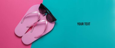 Yaz plajı konsepti. Güneş gözlükleri, pembe mavi arka planda parmak arası terlikler. Üst Manzara. Boşluğu kopyala