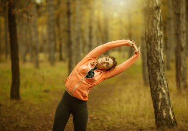 Spor giyim sektöründe genç ve çekici bir kadın sonbahar ormanlarında el egzersizi yapıyor. Koşmadan önce ısın. Sağlıklı yaşam tarzı kavramı