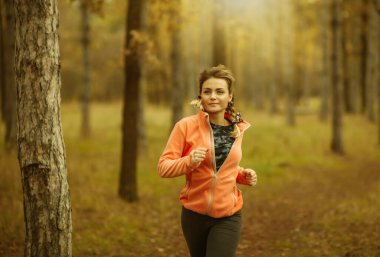 Sonbahar ormanında koşu. Spor giyimli genç bir kadın orman yolunda koşuyor. Sağlıklı yaşam tarzı kavramı